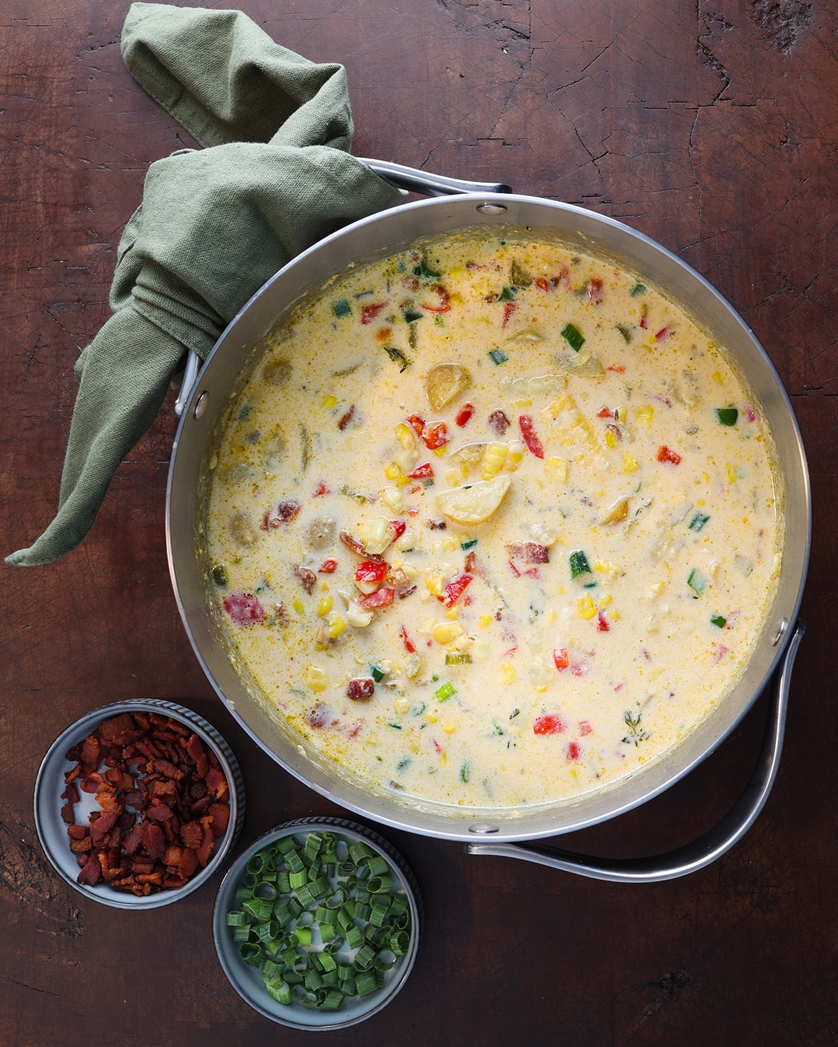 Large saucepan filled with a homemade fresh corn chowder with a sage green towel wrapped around the handle on the top side.